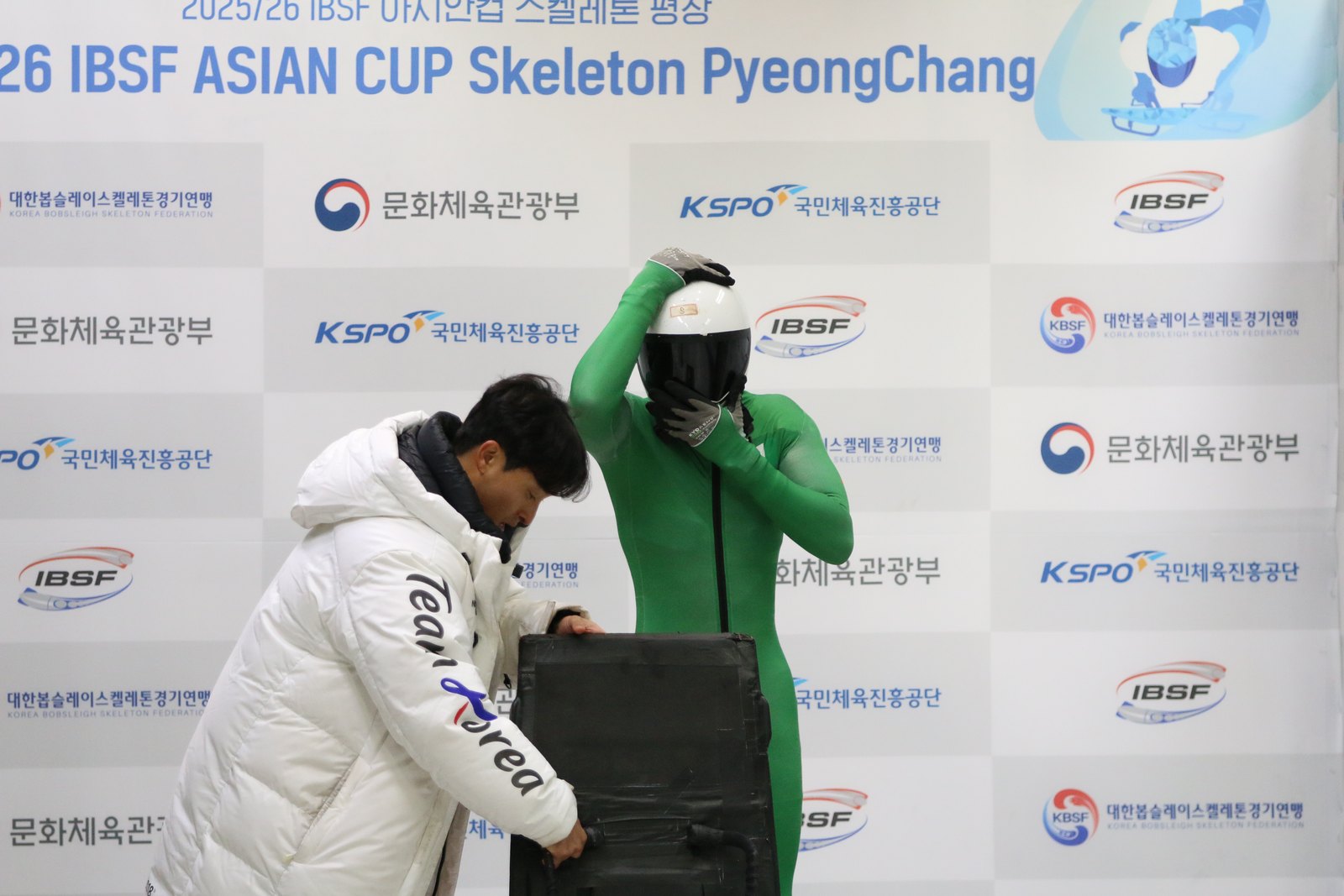 Yinka in the Nigeria green race suit at the 2025/26 IBSF Asian Cup skeleton competition in PyeongChang, taking his helmet off beside his sled
